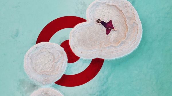 אישה בשמלה אדומה שוכבת על אי קטן של מלח במרכז מים בצבע תכלת, עם לוגו של אמות השקעות ברקע